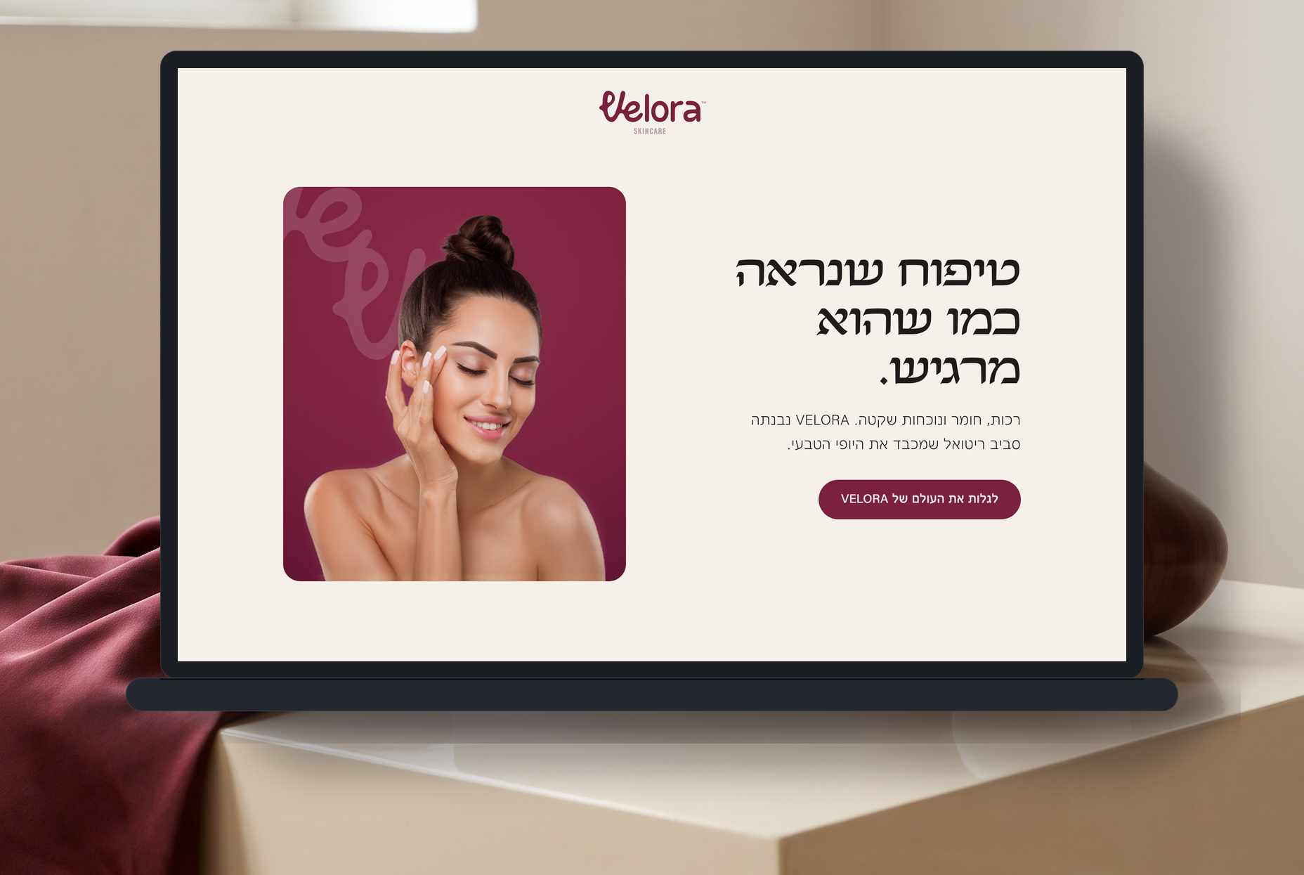 דף הנחיתה של VELORA מוצג על מסך מחשב בתוך סט בגוני קרם ובורדו