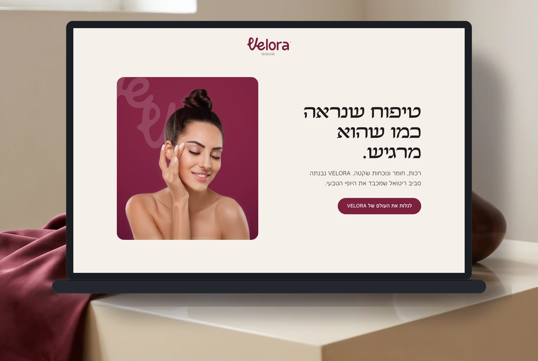 דף הנחיתה של VELORA מוצג על מסך מחשב בתוך סט בגוני קרם ובורדו